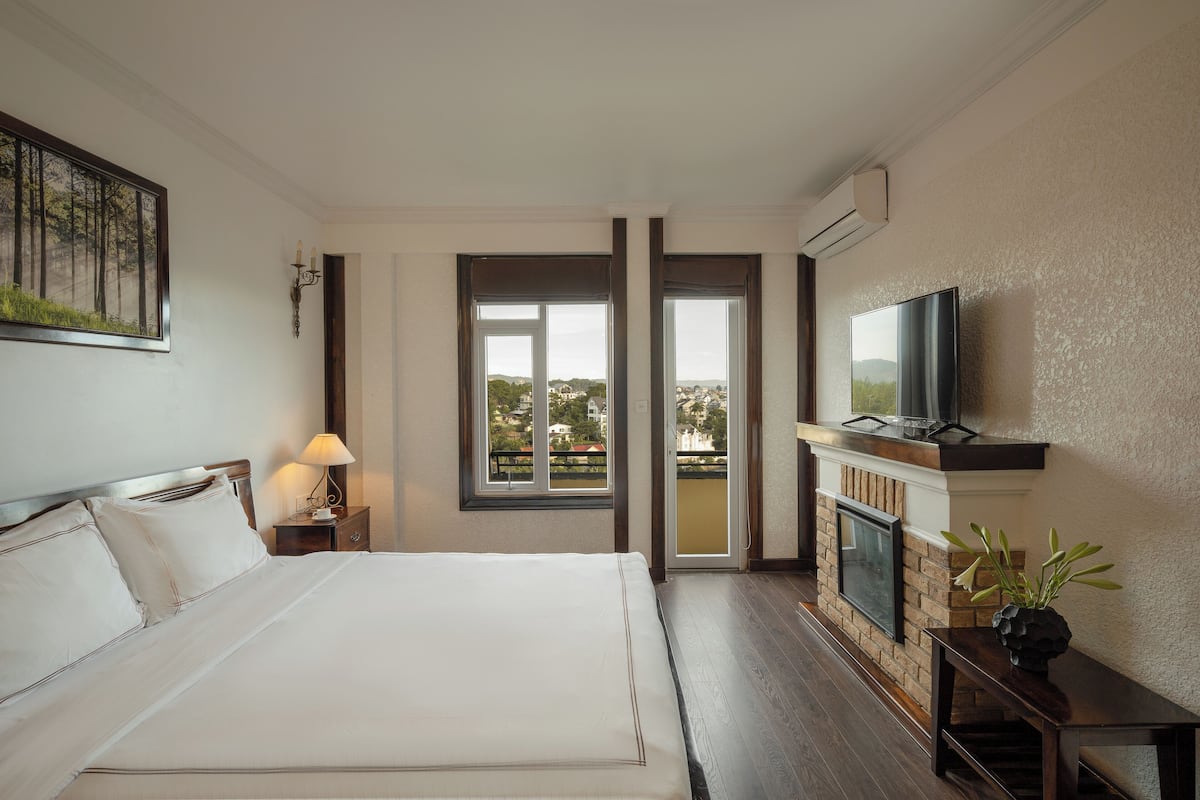 Habitación de hotel con una cama grande, televisión, chimenea y balcón con vistas.