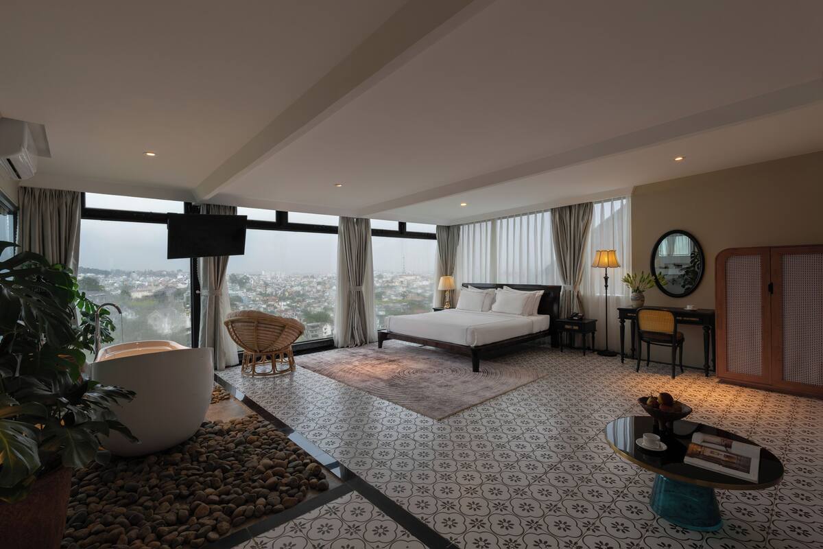 Habitación de hotel moderna con una cama grande, televisor de pantalla plana, mesa de comedor y vista a la ciudad.
