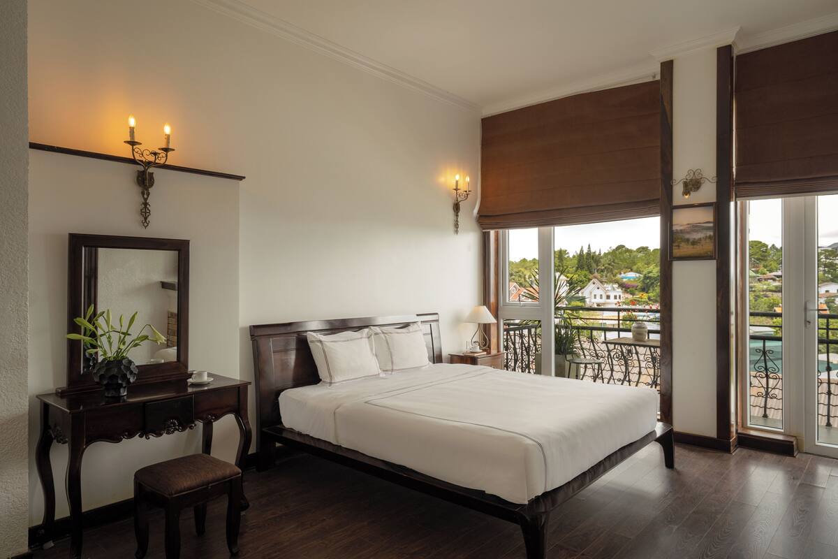Un dormitorio con una cama grande, un aparador, un espejo y una ventana con vista a un balcón.