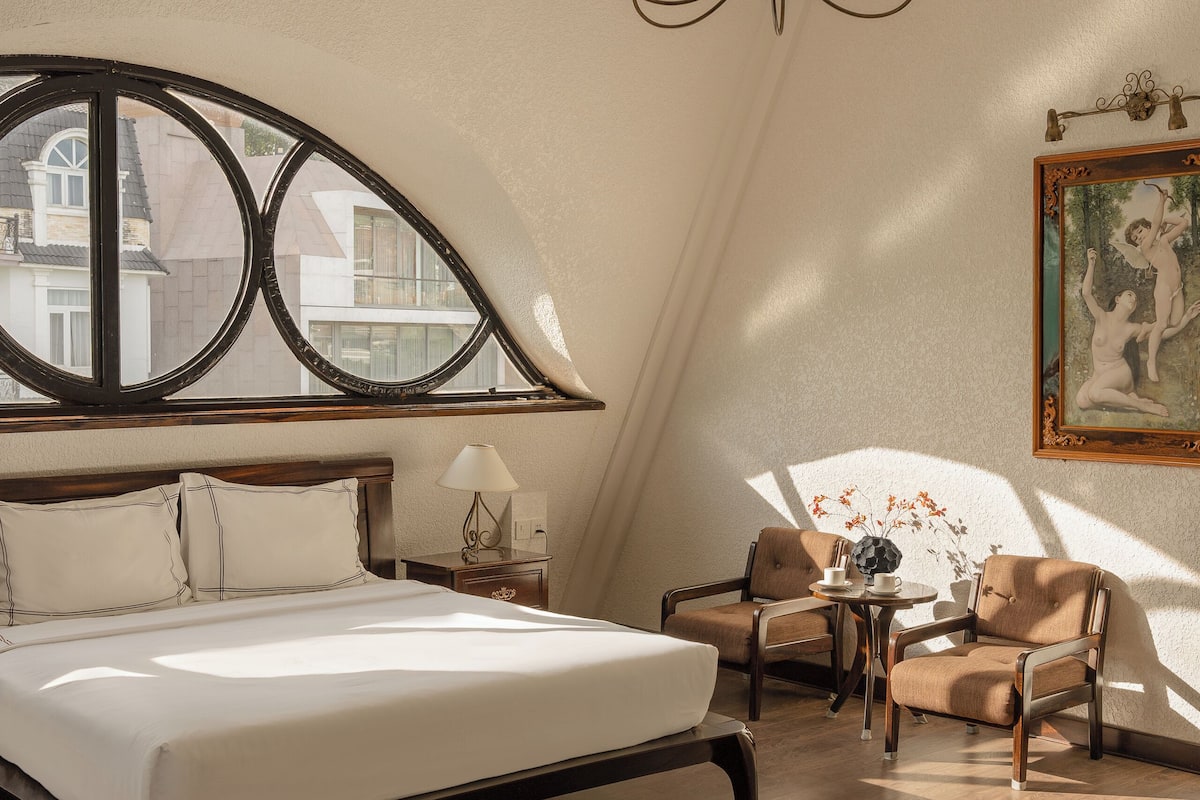 Un dormitorio con una cama grande, un candelabro, una ventana con vistas y un cuadro en la pared.
