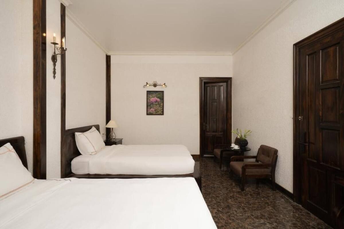 Habitación de hotel con dos camas, un espacio de descanso pequeño, una puerta y un cuadro colgado en la pared.