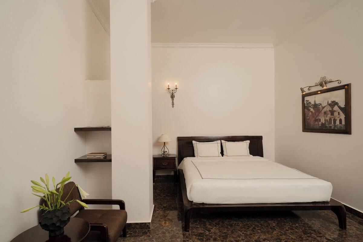 Un dormitorio ordenado con cama, mesita de noche, lámpara y un cuadro en la pared.