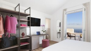 Une chambre d’hôtel avec un lit, un bureau avec une télévision, une armoire et un balcon avec vue.