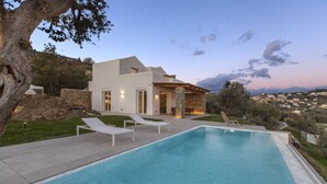 Une maison moderne dotée d’une piscine, de chaises longues et offrant une vue sur la ville.