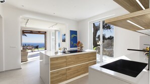 Une cuisine moderne dotée d’un grand îlot central, offrant une vue sur la mer, et d’un coin repas avec des sièges extérieurs.