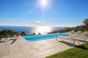 Ein Pool mit Meerblick, Liegestühle und ein Tisch mit Flasche und Glas.