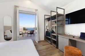 A hotel room with a bed, a desk with a laptop, a TV, a wardrobe, and a view of the sea. - MyExclusiveItaly - Design Villa with infinity pool & Li Galli view (Massa Lubrense)