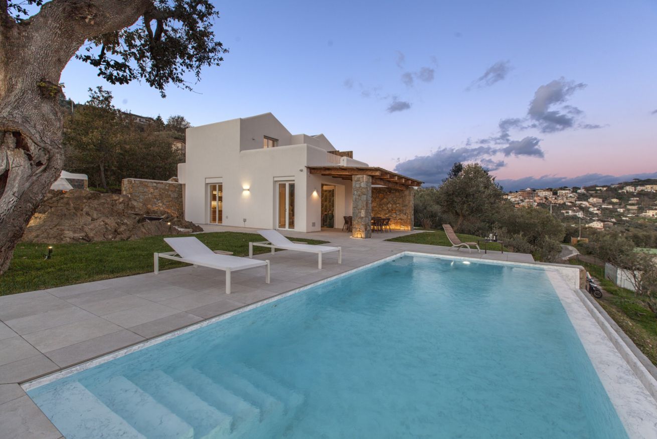 Una casa moderna con piscina, sillas de descanso y vistas al pueblo.