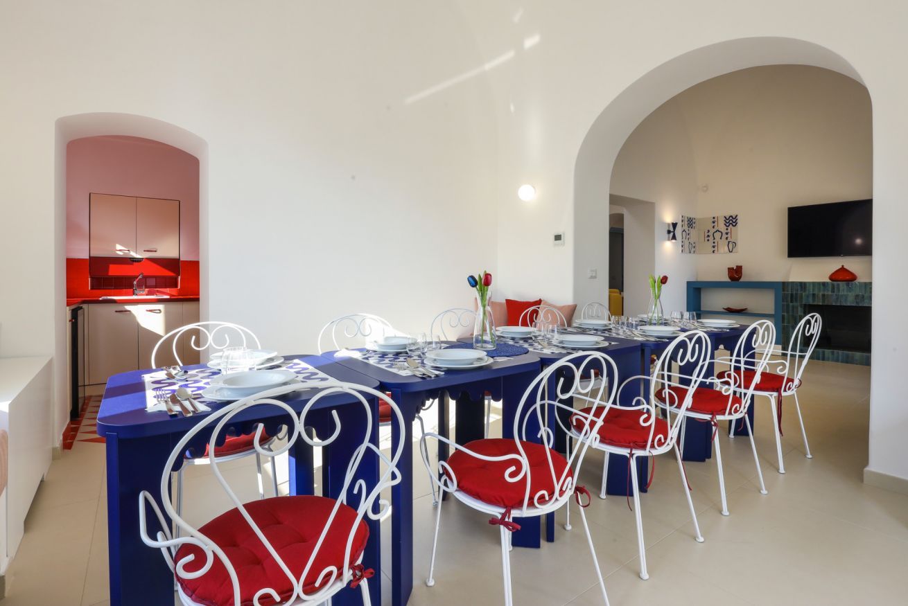 A dining area with a long table, white chairs with red cushions, and a blue tablecloth.