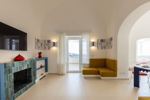 A modern living room with a fireplace, a sofa, a dining table, and a TV mounted on the wall. - MyExclusiveItaly - Elegant Villa in Anacapri | Infinity Pool & Design (Anacapri)
