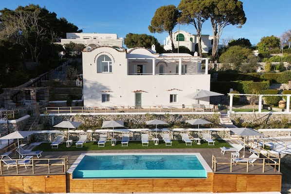 A white villa with a swimming pool, sun loungers, and umbrellas.