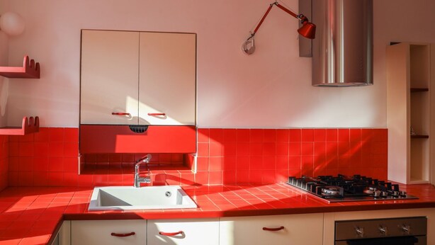A modern kitchen with red tiles, a stainless steel range hood, a gas stove, and a white sink.