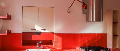 A modern kitchen with red tiles, a stainless steel range hood, a gas stove, and a white sink.
