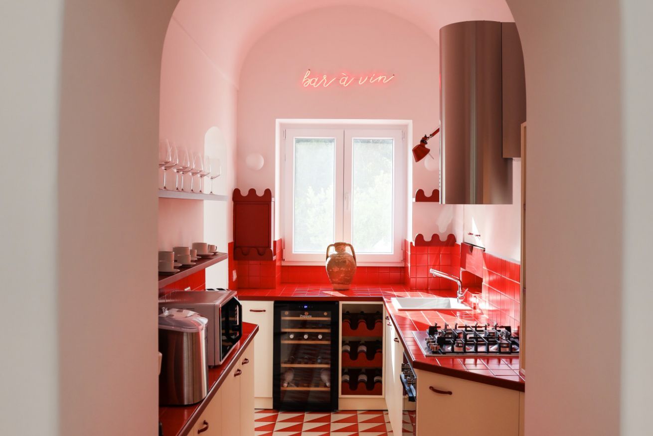 A kitchen with a red and white color scheme, a large window, and a neon sign that reads "bar à vin".