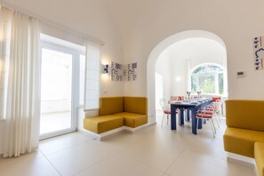 A modern living room with a sofa, dining table, and chairs. There is a large window and a door leading to an outdoor area. - MyExclusiveItaly - Elegant Villa in Anacapri | Infinity Pool & Design (Anacapri)