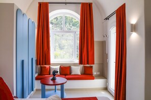 Ein Zimmer mit Fenster, roten Vorhängen, blauer Wand, rotem Sofa und einem runden Tisch.