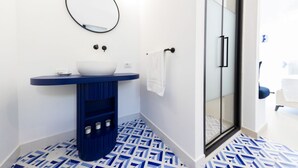 A bathroom with a white sink, blue vanity, patterned floor, and a glass shower door.