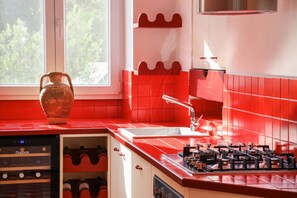 A kitchen with red tiles, a built-in wine cooler, and a window with a view of trees.