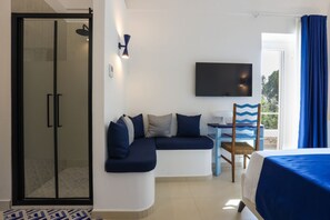 A modern hotel room with a curved sofa, a flat-screen TV, a small table, and a shower area.