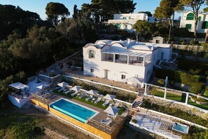 A white villa with a swimming pool, sun loungers, and a terrace.