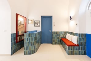 A bathroom with a blue door, a sink with a mirror, and a bench with pillows. - MyExclusiveItaly - Elegant Villa in Anacapri | Infinity Pool & Design (Anacapri)