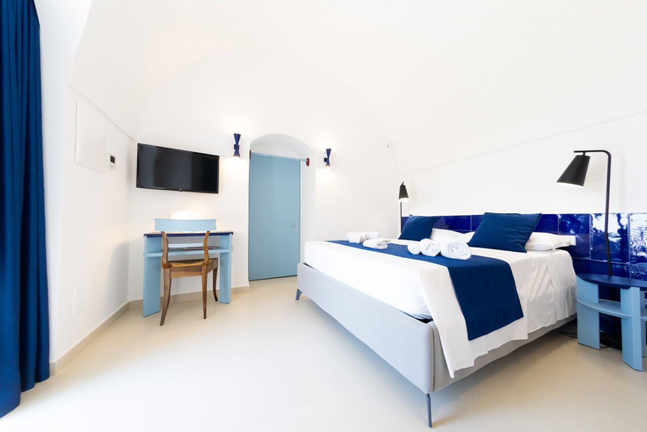 A bedroom with a bed, a desk, a chair, a TV, and a door.