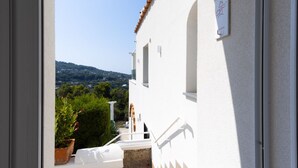 A white building with a stone staircase leading to a small outdoor area with a potted plant and a white bench.