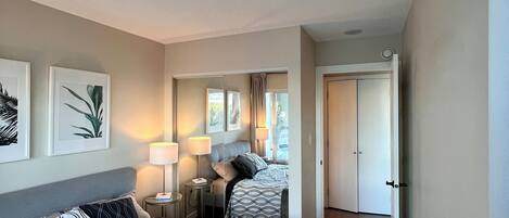 A hotel room with two beds, a sitting area with a chair and table, and a door leading to another room.