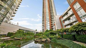 A modern high-rise building with a central courtyard featuring a reflective water feature and lush greenery.