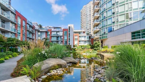 A modern apartment complex with a small garden pond, surrounded by lush greenery and large windows.