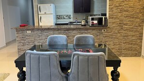Een moderne keuken met een granieten aanrecht, een koelkast, een magnetron en een kast. Er staat een eettafel met twee stoelen voor de keuken.