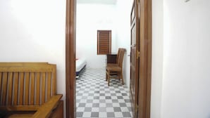 A narrow hallway with a checkered floor, a wooden bench on the left, and a chair on the right.