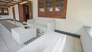 A room with a white sofa, a white armchair, and a small table. There is a window with wooden frames and a door leading outside.
