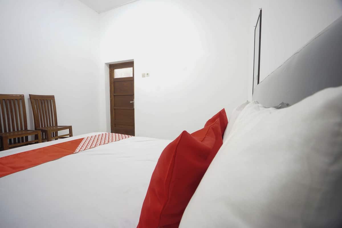 Een slaapkamer met een bed, een houten deur en twee houten stoelen.