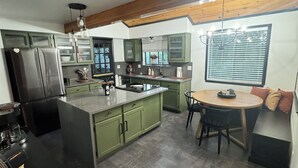 A modern kitchen with green cabinets, a central island, and a dining area with a round table. - Hot tub, Sauna, adult game room, pool table, house has lots of stairs! (Reno)