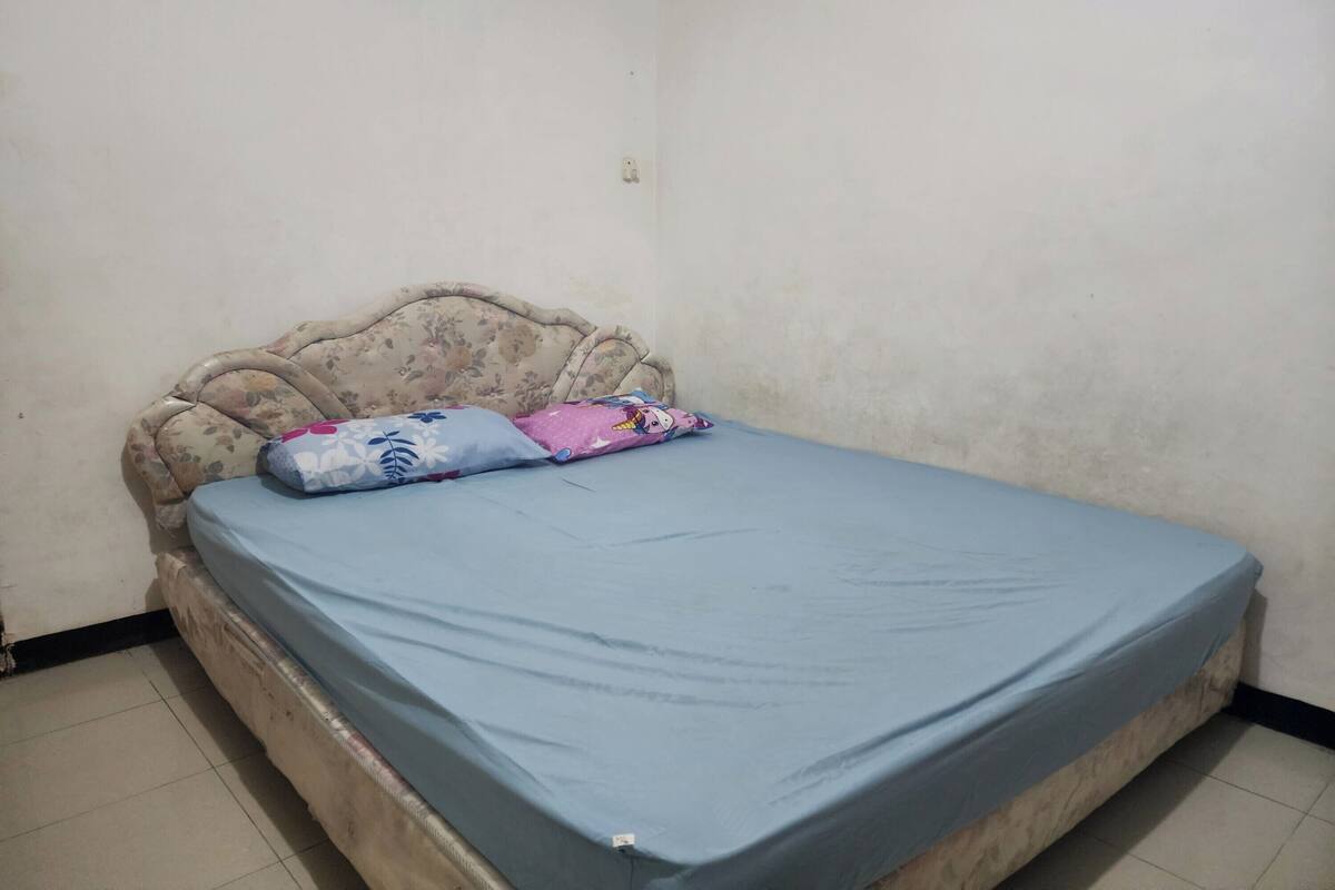 A single bed with a floral headboard, a blue mattress cover, and two pillows with cartoon designs.