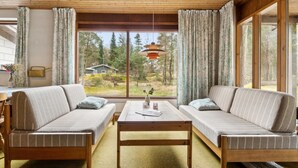 Un salon chaleureux avec deux canapés, une table basse en bois et de grandes fenêtres donnant sur une maison et des arbres.