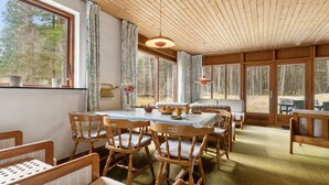 Une pièce chaleureuse, dotée de meubles en bois, de grandes fenêtres et d’un plafond avec des poutres apparentes.