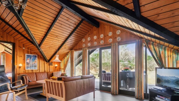 Un intérieur de chalet chaleureux avec un plafond en bois, un canapé, une table à manger et un téléviseur.