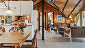 Une cuisine spacieuse avec un plafond en bois, un coin repas avec une table et des chaises en bois, et un salon avec un canapé et un tableau au mur.