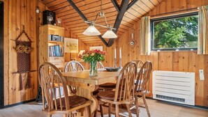 L’intérieur d’un chalet en bois comprend une table à manger, des chaises, une bibliothèque et une fenêtre donnant sur la forêt.