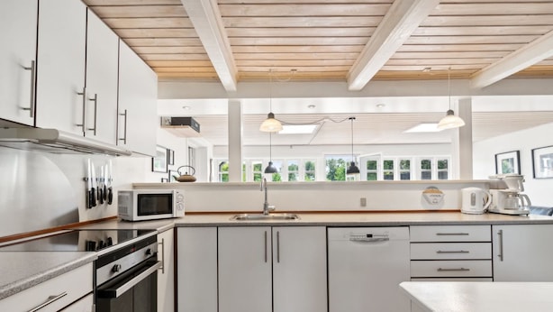 Une cuisine moderne avec des meubles blancs, des appareils en acier inoxydable et un plafond en bois.