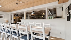 Un espace repas avec une longue table en bois et des chaises blanches dotées de coussins foncés.