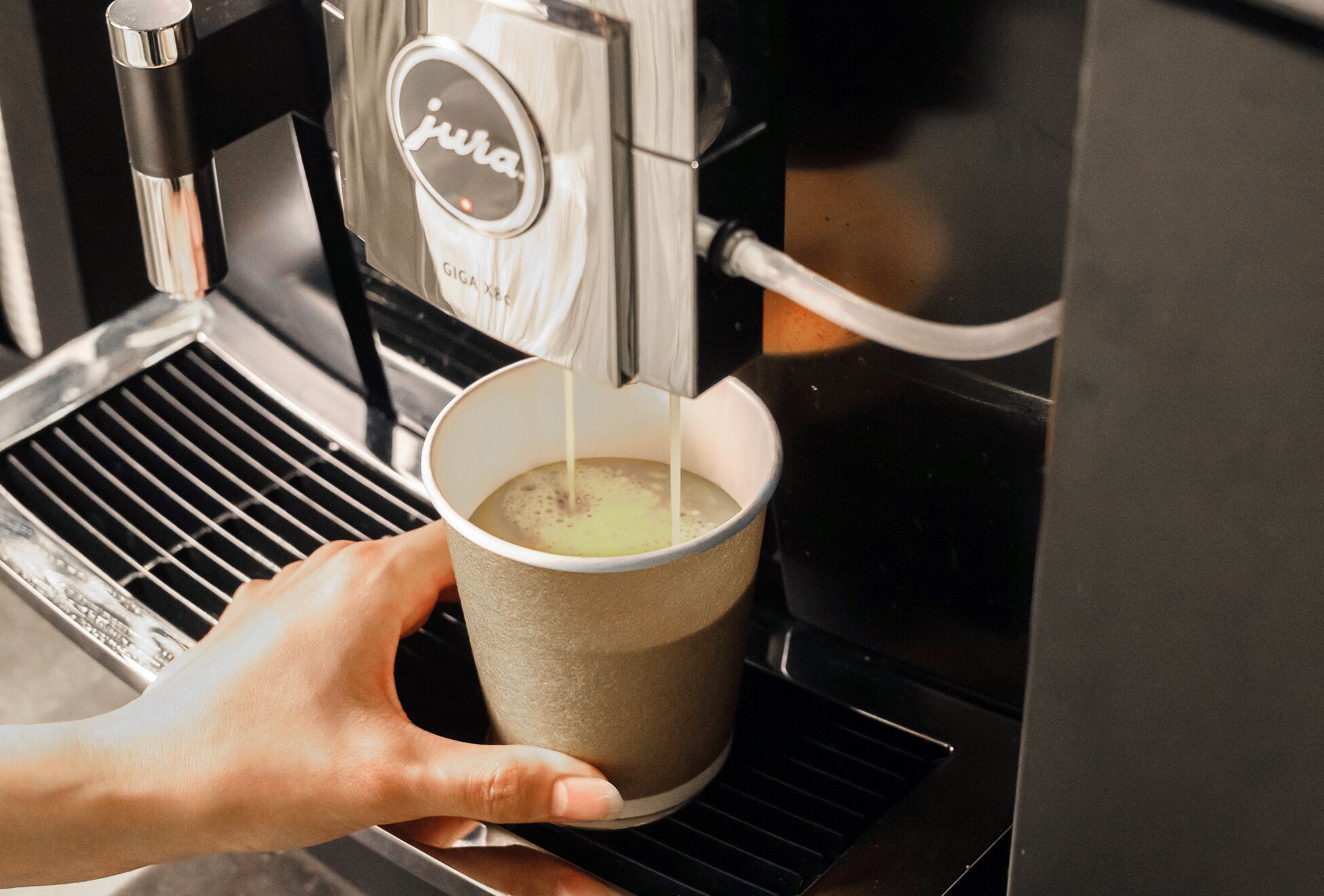 Una mano sosteniendo una taza debajo de una máquina de café que sirve café.