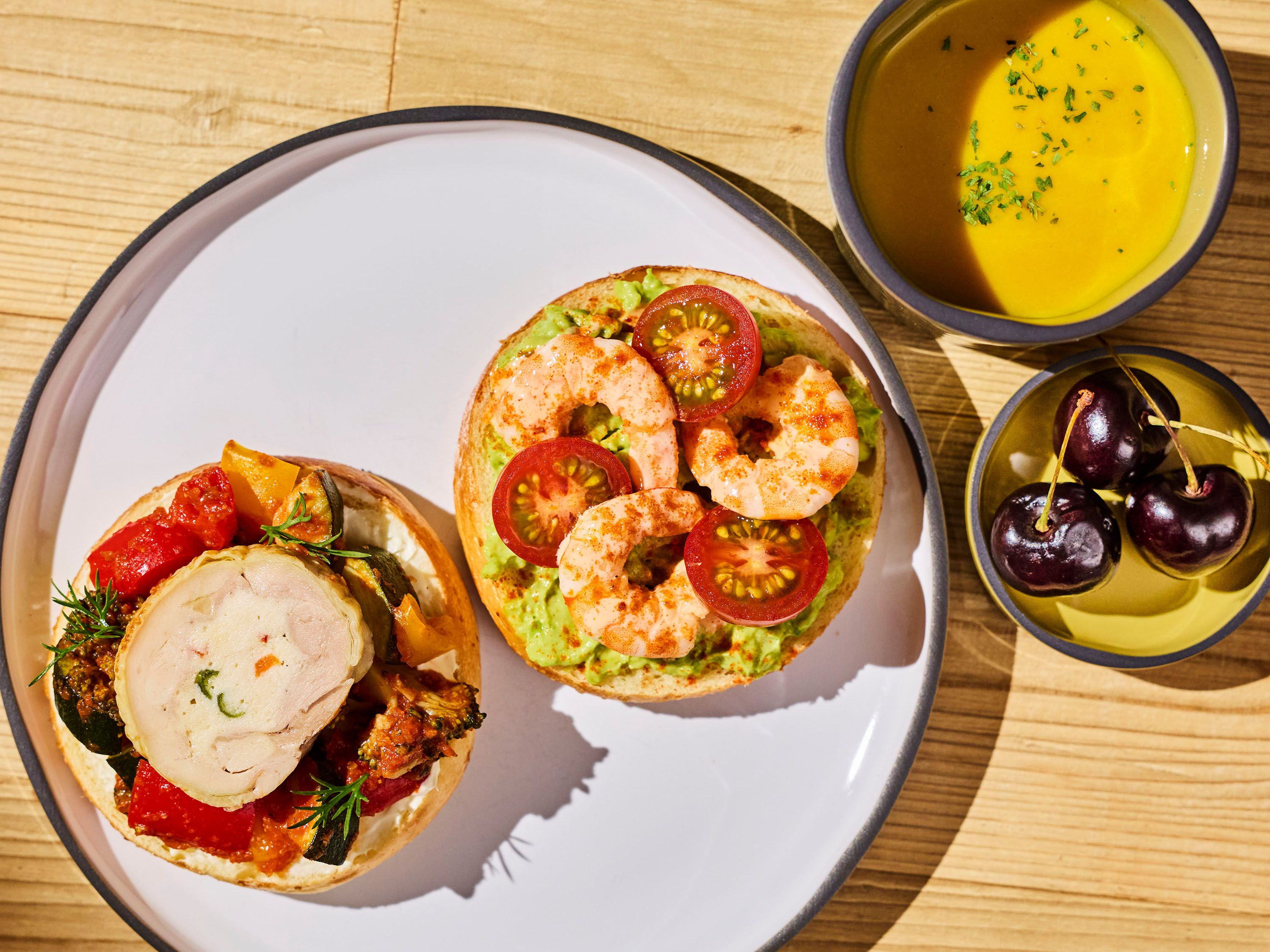 Une assiette avec deux sandwichs ouverts, un bol de soupe et une assiette de cerises.