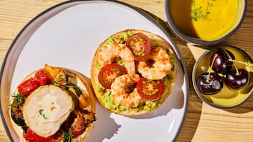 A plate with two open-faced sandwiches, a bowl of soup, and a plate with cherries.