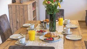 A breakfast table with plates, cups, a vase with flowers, and a glass of orange juice. - Ferienwohnung Kampenwand (Bernau am Chiemsee)