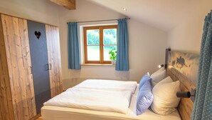 A bedroom with a bed, wooden wardrobe, a window with curtains, and a view of greenery outside. - Ferienwohnung Kampenwand (Bernau am Chiemsee)
