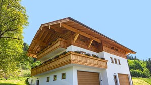 A two-story chalet with wooden balconies, a garage, and a garden setting. - Ferienwohnung Kampenwand (Bernau am Chiemsee)