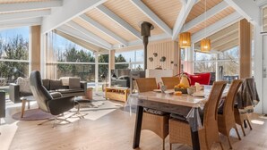 A spacious living area with a wooden floor, a dining table with wicker chairs, a red sofa, and a large window offering a view of trees. - "Anastaja" - 550m from the sea by Interhome (Jerup)